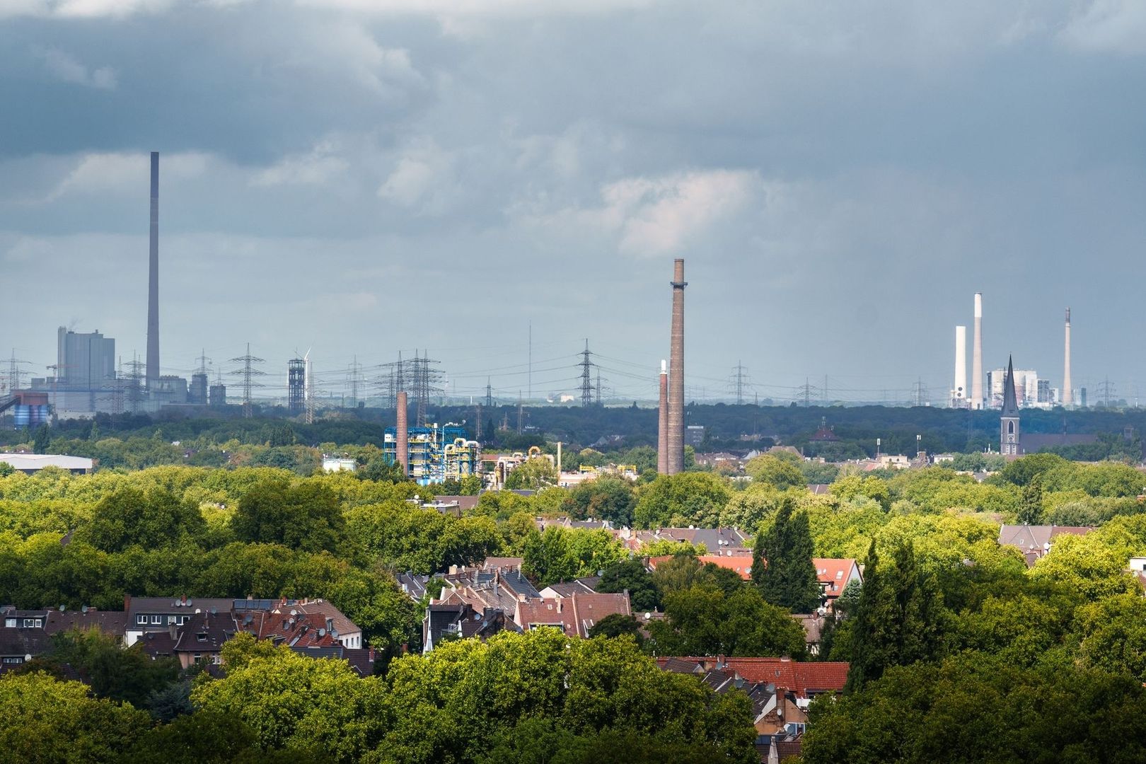 Industrieel landschap met fabrieksschoorstenen boven een groene woonwijk